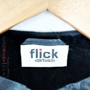 May include: A white tag with black text that reads "flick (aktuell)" on a black fabric background.