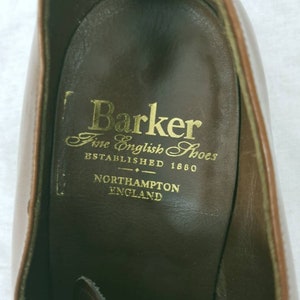 May include: Close-up of the inside of a brown leather shoe with the Barker Fine English Shoes logo. The logo reads "Barker Fine English Shoes Established 1880 Northampton England."