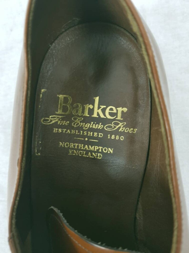 May include: Close-up of the inside of a brown leather shoe with the Barker Fine English Shoes logo. The logo reads "Barker Fine English Shoes Established 1880 Northampton England."
