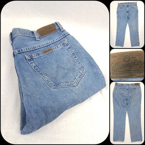 May include: A pair of blue denim jeans with a brown leather Wrangler label. The label has the Wrangler logo and the text "Wrangler Durable Quality".