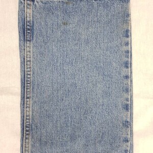 May include: Close-up of the denim fabric of a pair of blue jeans. The fabric has a light blue color and a woven texture.