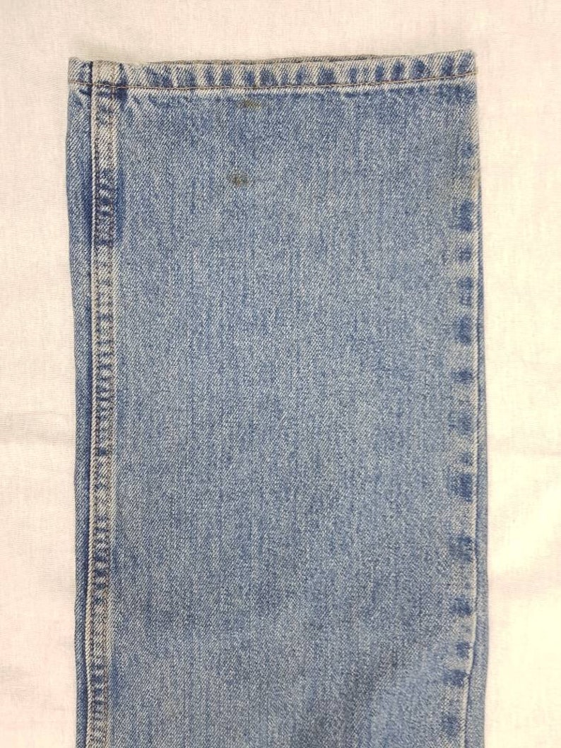 May include: Close-up of the denim fabric of a pair of blue jeans. The fabric has a light blue color and a woven texture.