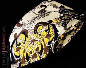 May include: A beige silk tie with a yellow, brown, and black paisley pattern. The tie is folded in half and the pattern is visible on both sides.