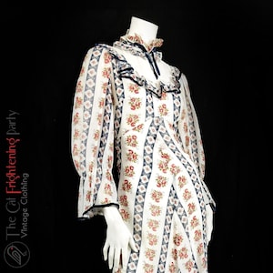May include: A white maxi dress with a floral print and blue trim. The dress has a ruffled collar and long sleeves.