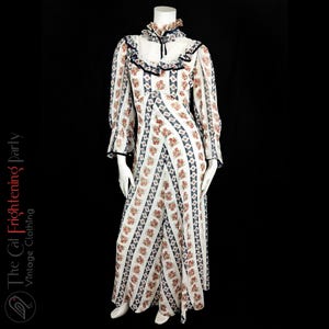 May include: A white maxi dress with a floral print and blue and red accents. The dress has a high neck with a ruffle collar and long sleeves with ruffles at the cuffs.