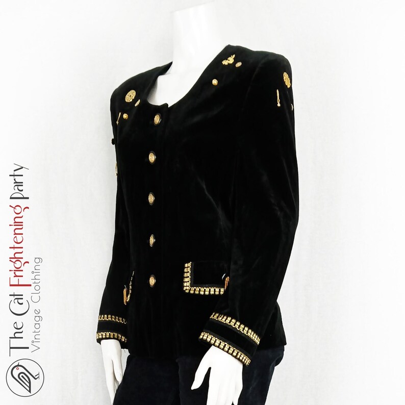 May include: A black velvet blazer with gold buttons and trim. The blazer has a stand-up collar and long sleeves.