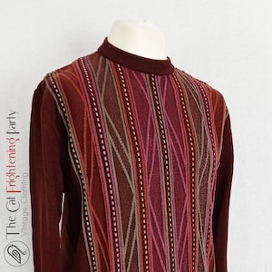 Puede incluir: Un suéter marrón con un patrón a rayas en tonos de rojo, rosa y verde. El suéter tiene cuello redondo y mangas largas.