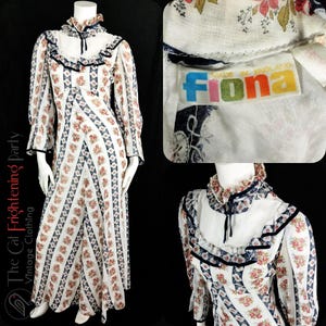 May include: A white maxi dress with a floral print and a blue and white geometric pattern. The dress has a high neck with a ruffle collar and long sleeves. The dress is made by Fiona and is made in England.