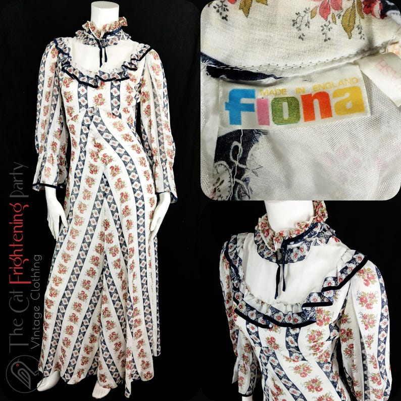 May include: A white maxi dress with a floral print and a blue and white geometric pattern. The dress has a high neck with a ruffle collar and long sleeves. The dress is made by Fiona and is made in England.