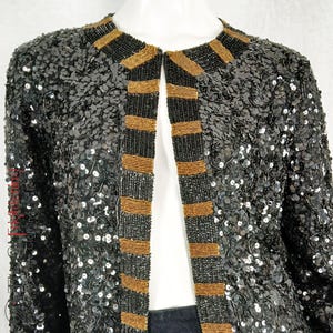 May include: A black sequined jacket with gold beaded trim. The jacket has a long, open front and a collarless neckline.
