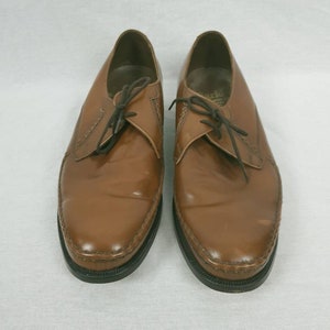 May include: A pair of brown leather lace-up shoes with a pointed toe and a black rubber sole.