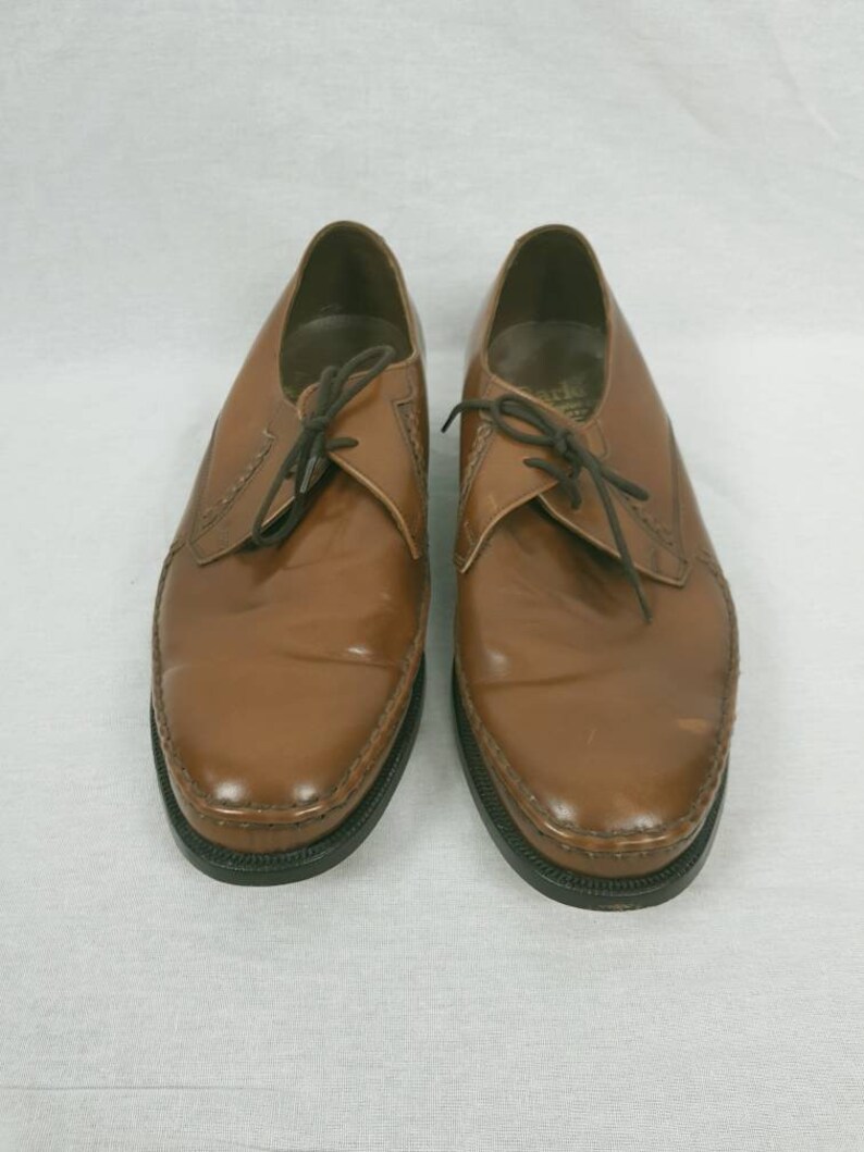 May include: A pair of brown leather lace-up shoes with a pointed toe and a black rubber sole.