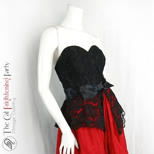Può includere: Abito senza spalline con corpetto in pizzo nero e gonna rossa. L'abito presenta un fiocco in raso nero in vita e un'applicazione in pizzo nero sulla gonna. Il logo The Cat Frightening Party Vintage Clothing è visibile.