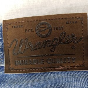 May include: A brown leather patch with the text "Trade Mark Est. 1947 Wrangler Durable Quality" in black lettering.