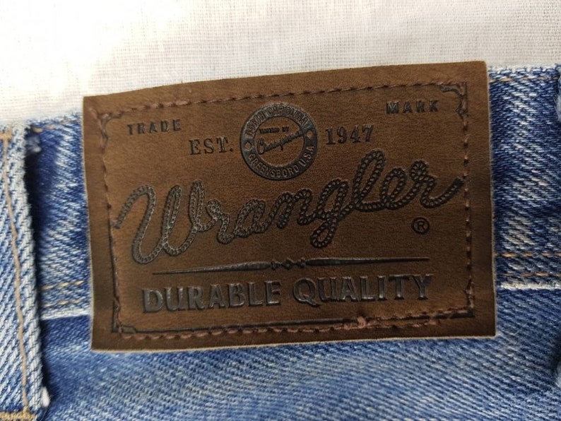 May include: A brown leather patch with the text "Trade Mark Est. 1947 Wrangler Durable Quality" in black lettering.