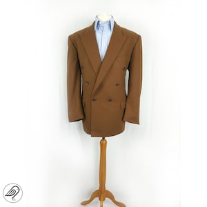 May include: A brown double-breasted blazer with a light blue button-down shirt underneath. The blazer is on a wooden mannequin stand.