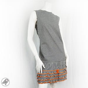 May include: A sleeveless black and white gingham dress with a ruffled hem. The ruffles are trimmed with orange ribbon.