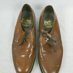 May include: A pair of brown leather lace-up shoes with a black sole. The shoes have a label on the inside that reads "Barker Fine English Shoes Established 1880 Northampton England".