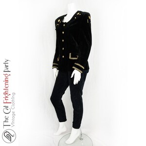 May include: A black velvet blazer with gold trim and buttons. The blazer has a stand-up collar and long sleeves.