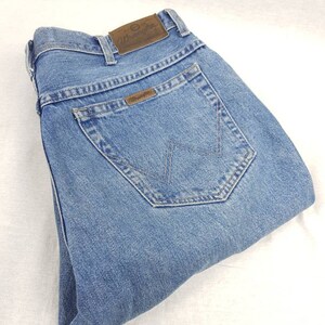 May include: A pair of light blue denim jeans with a brown leather Wrangler label on the back pocket.