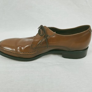 May include: A brown leather dress shoe with a lace-up closure. The shoe has a black sole and a slightly pointed toe.