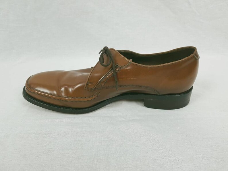 May include: A brown leather dress shoe with a lace-up closure. The shoe has a black sole and a slightly pointed toe.
