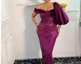 May include: A woman wearing a purple sequined gown with a one-shoulder design and a large, puffy sleeve. The gown has a fitted bodice and a flowing skirt. She is also wearing a purple head wrap.