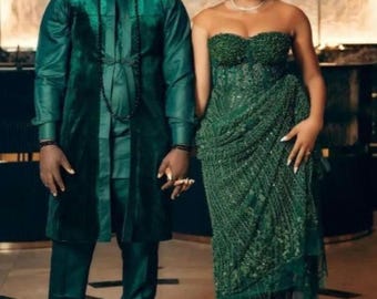 May include: A couple in matching emerald green outfits. The woman is wearing a beaded strapless dress and a head wrap. The man is wearing a long-sleeved shirt, pants, and a cap. They are standing together, holding hands.