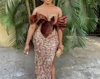 May include: A woman wearing a brown velvet and lace dress with a gold head wrap. The dress has a sweetheart neckline and a high slit on the side. She is holding a small clutch purse.