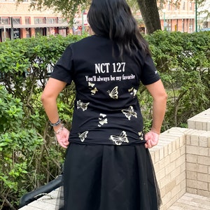 Peut inclure: T-shirt noir avec des motifs de papillons dor&eacute;s et le texte "NCT 127 You'll always be my favorite".