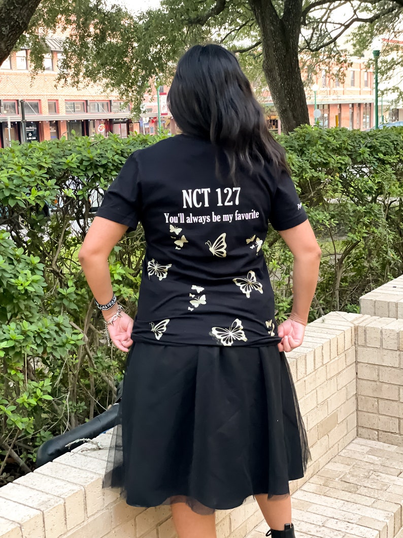 Peut inclure: T-shirt noir avec des motifs de papillons dor&eacute;s et le texte "NCT 127 You'll always be my favorite".