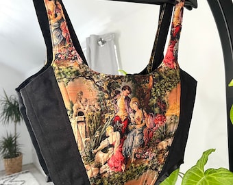 May include: A black corset with a floral print featuring a scene of people in a garden. The corset has adjustable straps and a boned bodice.