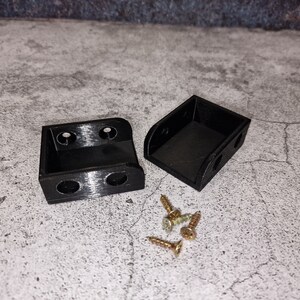 May include: Two black plastic corner brackets with four screw holes each, and four small gold screws.