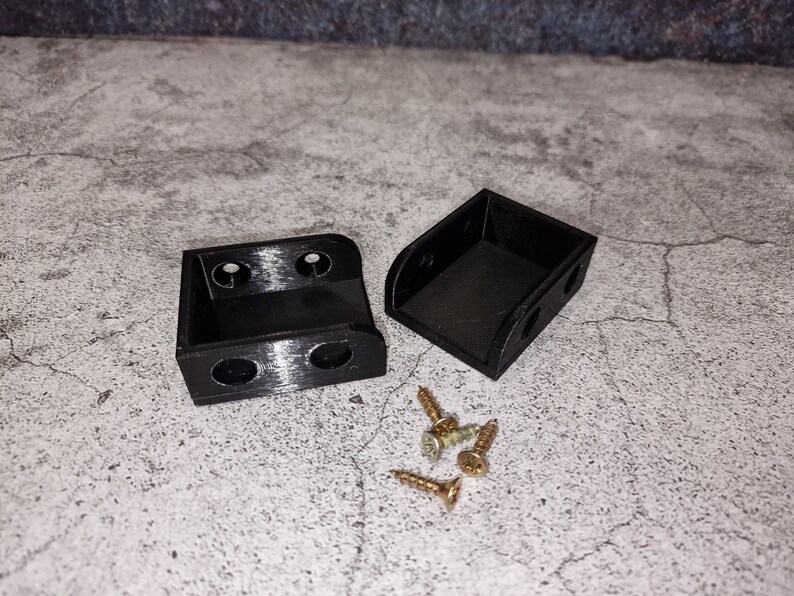 May include: Two black plastic corner brackets with four screw holes each, and four small gold screws.