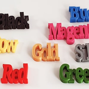 May include: A collection of 3D printed words representing different colors, including black, yellow, red, gold, blue, magenta, silver, and green.