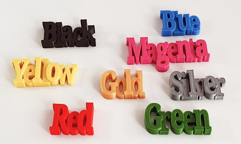 May include: A collection of 3D printed words representing different colors, including black, yellow, red, gold, blue, magenta, silver, and green.