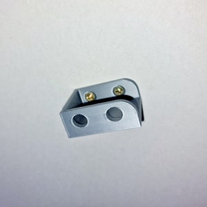 May include: A gray plastic bracket with two holes and two screws. The bracket is designed to be mounted to a wall or other surface.