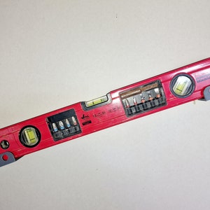 May include: A red level with a built-in screwdriver set. The level has two bubble vials and a black and gray handle. The screwdriver set includes a variety of bits for different screw sizes.