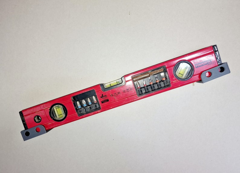 May include: A red level with a built-in screwdriver set. The level has two bubble vials and a black and gray handle. The screwdriver set includes a variety of bits for different screw sizes.
