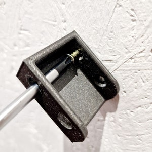 May include: A black plastic wall mount with a screw inserted into it. A screwdriver is being used to tighten the screw.