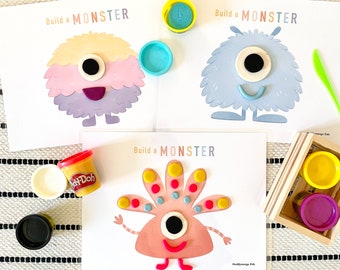 May include: Three printable monster activity cards with the text "Build a Monster" and images of monsters with different colors and shapes. The cards are designed for children to use playdough to create their own monsters.