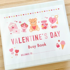 May include: White binder with a Valentine's Day themed cover. The cover features illustrations of hearts, a teddy bear, and the text "VALENTINE'S DAY Busy Book". Includes space to write "Belongs to..."
