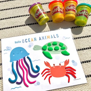 May include: A printable activity sheet with the text "Hello OCEAN ANIMALS" at the top. The sheet features a jellyfish, a turtle, and a crab. The animals are outlined and ready for children to fill in with Play-Doh.