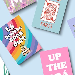 May include: A collection of greeting cards with various designs and text. One card features a rainbow background with the text "L&aacute; breithe sona duit" and a cake illustration. Other cards have phrases like "FARTS" and "UP THE GR&Aacute;".