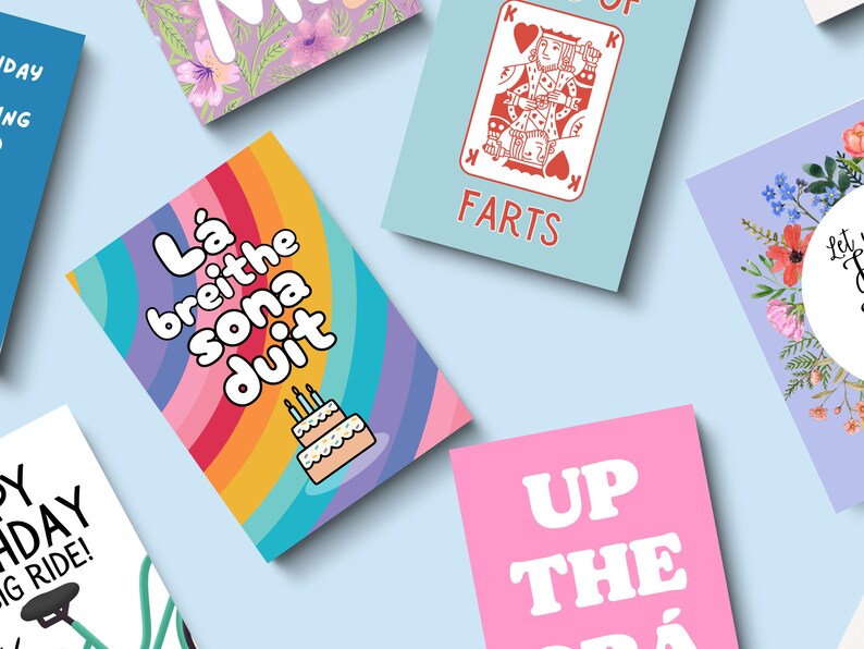 May include: A collection of greeting cards with various designs and text. One card features a rainbow background with the text "L&aacute; breithe sona duit" and a cake illustration. Other cards have phrases like "FARTS" and "UP THE GR&Aacute;".