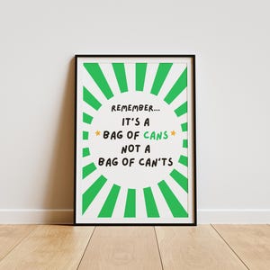 Könnte beinhalten: Gerahmter Druck mit schwarzem Rahmen, der eine motivierende Botschaft zeigt. Der Text lautet "Remember... It's a bag of cans not a bag of can'ts" in einer verspielten Schriftart, umgeben von einem grünen Sonnenstrahl-Design.