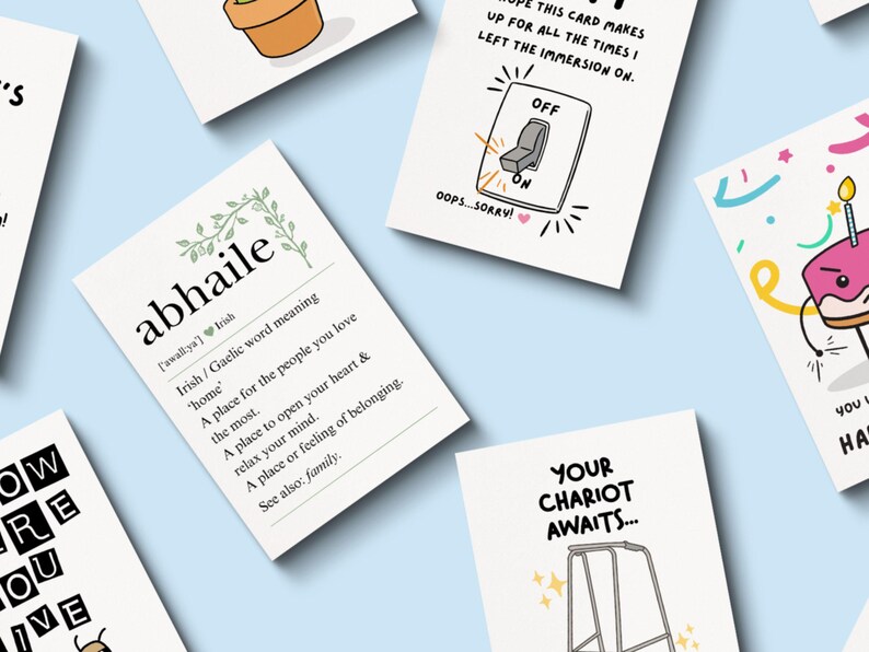 May include: A collection of greeting cards with various designs and text on a light blue background. One card features the word "abhaile" with an Irish definition. Other cards have illustrations of a light switch, a cake, and a walker.