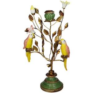Op de afbeelding: Een decoratieve kandelaar met een goudkleurig metalen boomontwerp, met gele en roze papegaaien op takken. De basis en een centrale beker zijn groen. Witte bloemen en gouden bladeren maken het ontwerp compleet.
