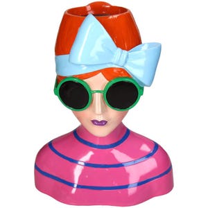 May include: A ceramic planter shaped like a woman's bust. The woman has red hair, a blue bow, green sunglasses, and a pink and blue striped shirt.