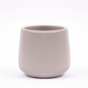Può includere: Un vaso in ceramica di colore grigio chiaro con forma arrotondata. Il vaso è vuoto e pronto per una pianta.